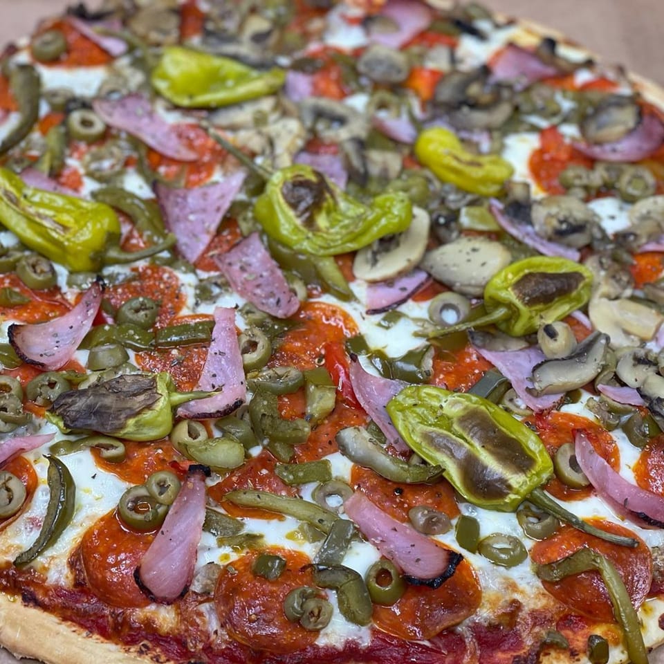Close-up of a Peppy's Pizza with pepperoni, green peppers, olives, mushrooms, and red onions.