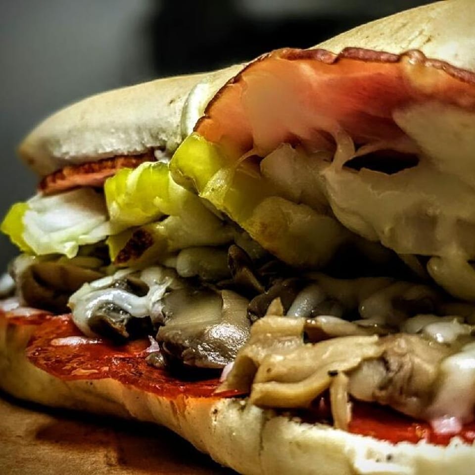 Close-up of a Peppys Pizza sub sandwich filled with meat, lettuce, mushrooms, and sauce.