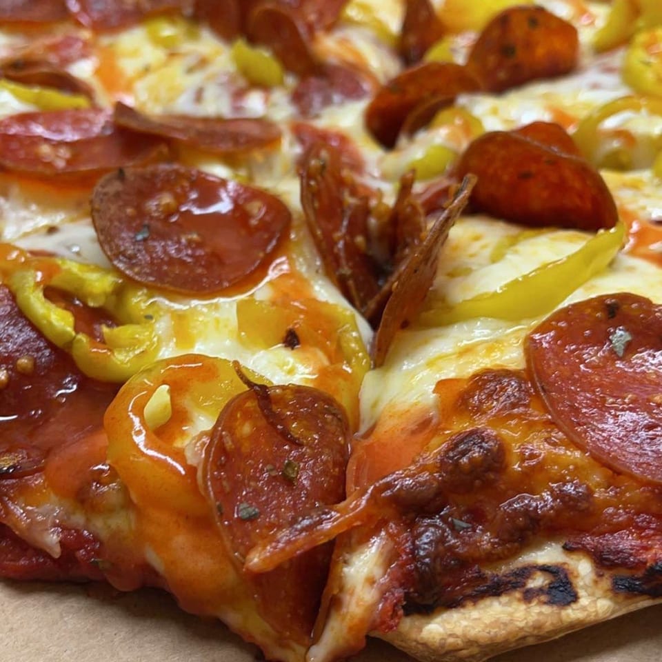 Close-up of a Peppy's Pizza slice with pepperoni, melted cheese, and banana peppers.