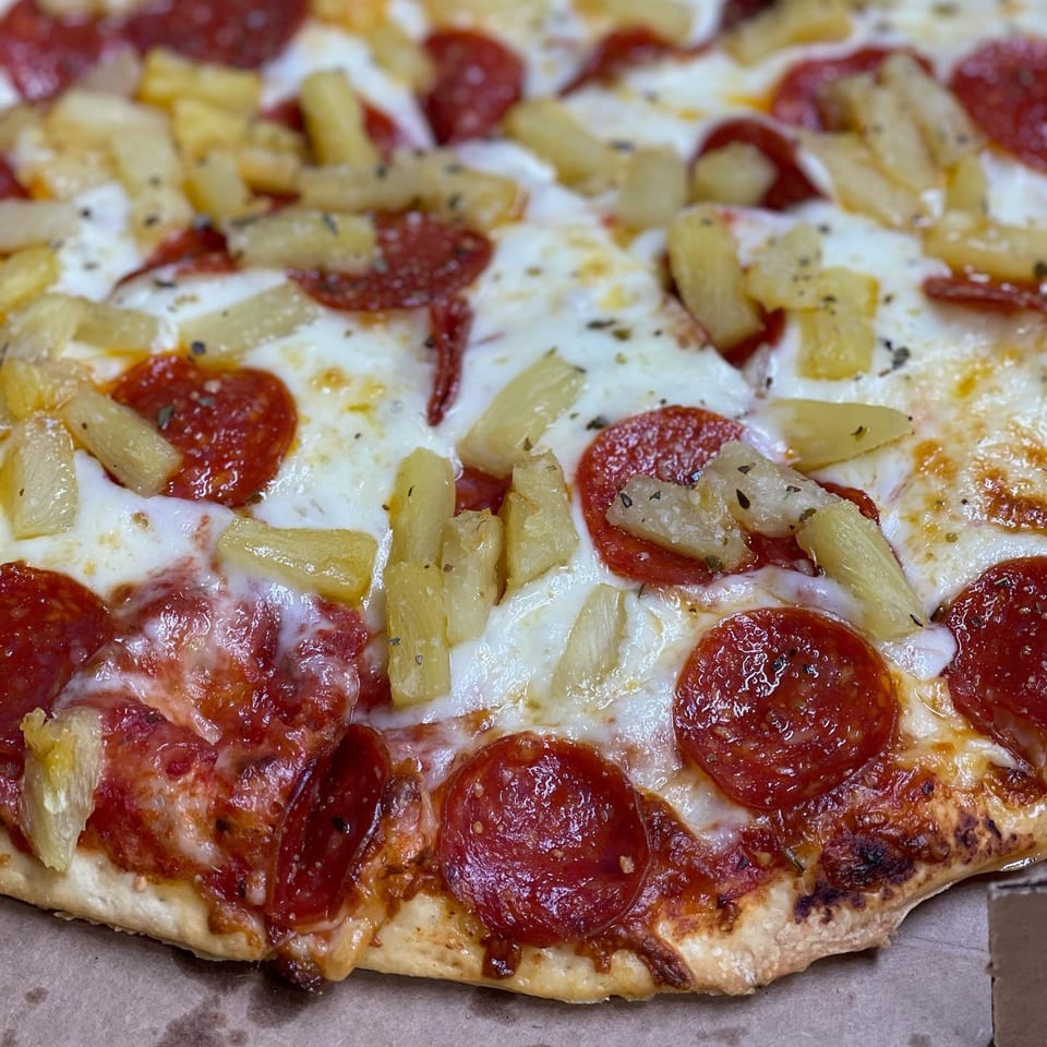 Close-up of a Peppy's Pizza with pepperoni, pineapple, and melted cheese.