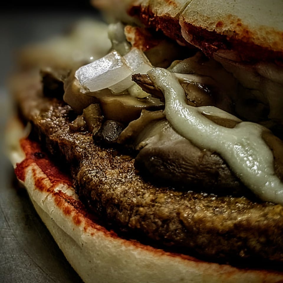 Close-up of a Peppys Pizza sandwich with steak, melted cheese, onions, and mushrooms.