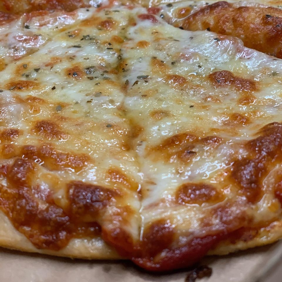 Close-up of a Peppys Pizza, showing melted cheese, herbs, and a golden-brown crust.